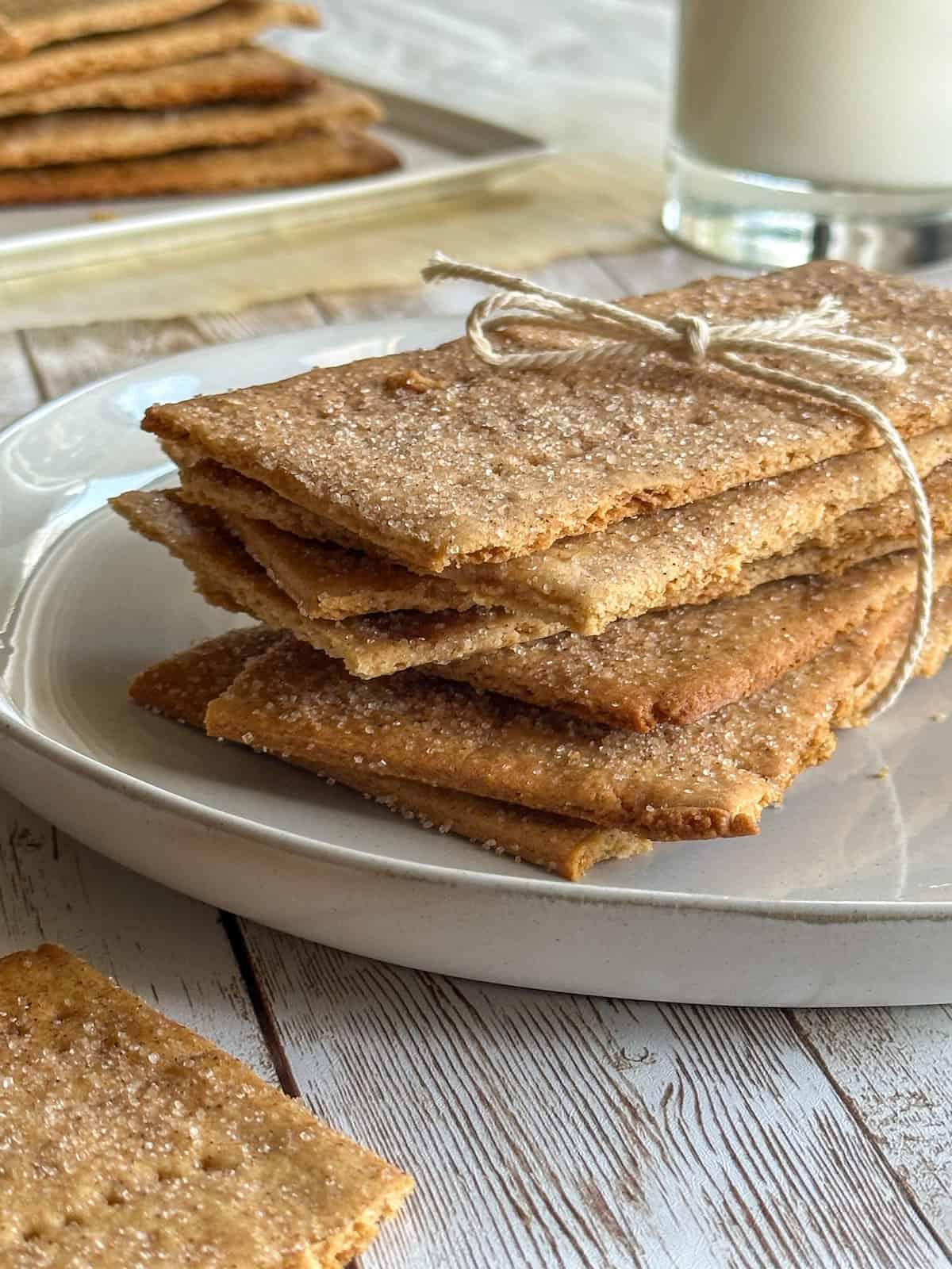 soudough graham crackers on a plate. The crackers are stacked on top of one another and tied with a piece of kitchen twine. There is a glass of milk in the background.
