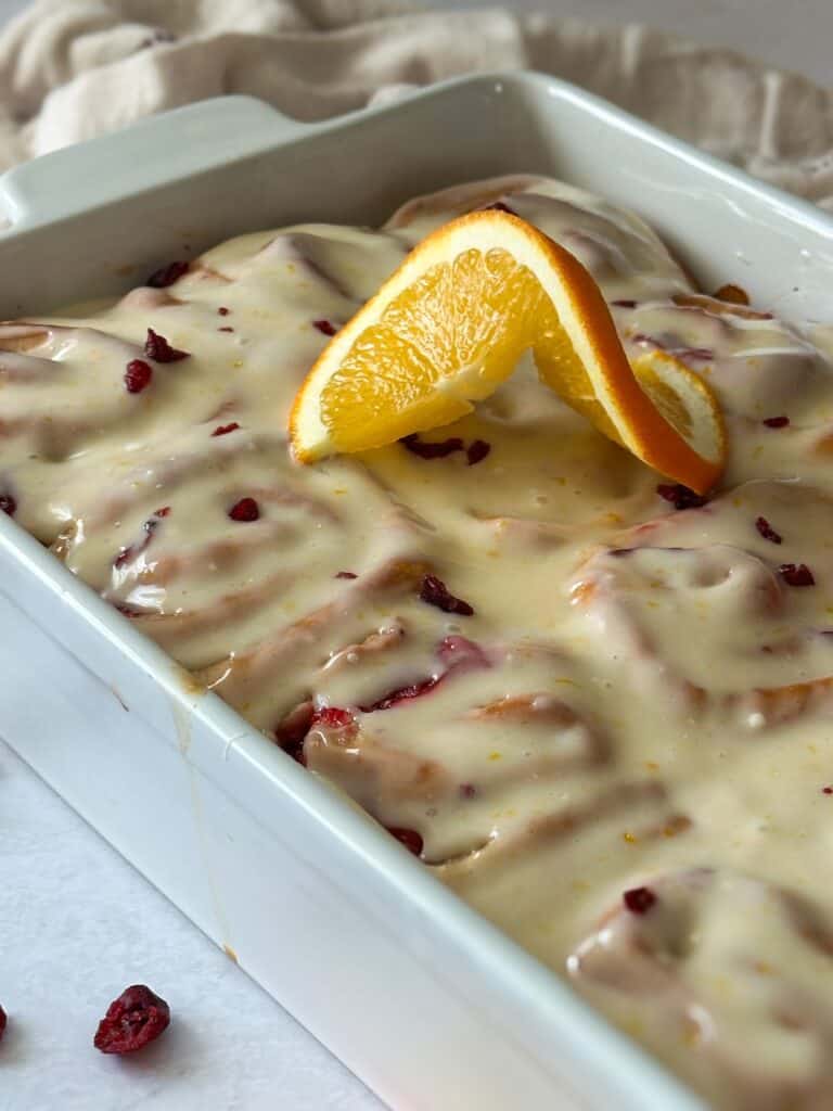 Finished sourdough cranberry orange rolls in baking pan, garnished with an orange slice.