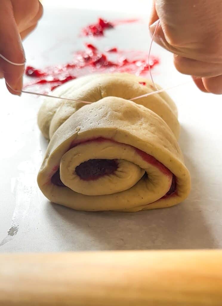 Hands using a piece of dental floss to cut the sourdough cinnamon rolls into individual rolls.