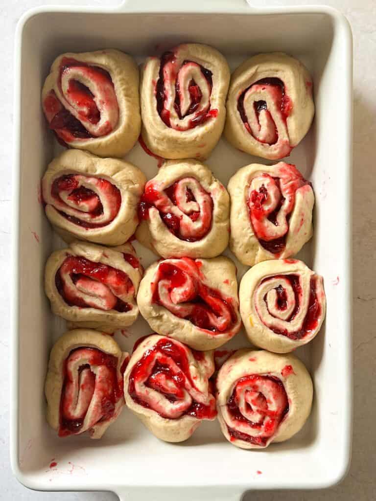 sourdough cranberry orange rolls in baking pan after second proof. They appear puffy and are touching each other.