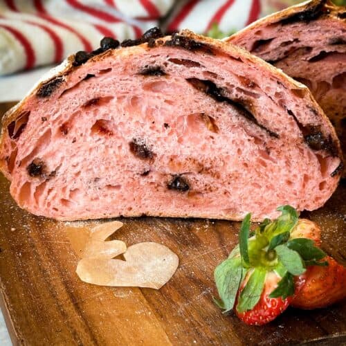 Chocolate strawberry sourdough bread loaf cut in half to reveal the crumb. The crumb is filled with dark chocolate chips and strawberries.