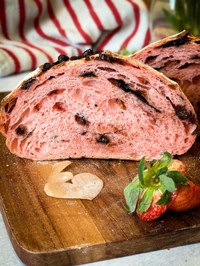 Chocolate strawberry sourdough bread loaf cut in half to reveal the crumb. The crumb is filled with dark chocolate chips and strawberries.
