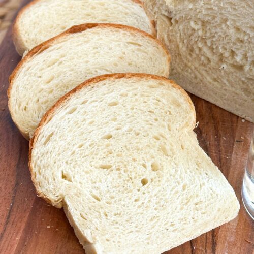 sourdough discard sandwich bread that is partially sliced into several slices on a wood cutting board.