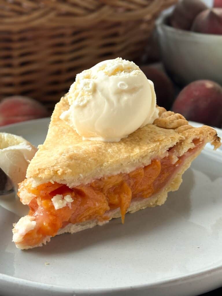 A plate with a slice of peach pie with a scoop of vanilla ice cream on top. 