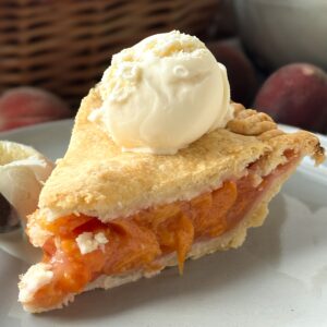 A plate with a slice of peach pie with a scoop of vanilla ice cream on top.