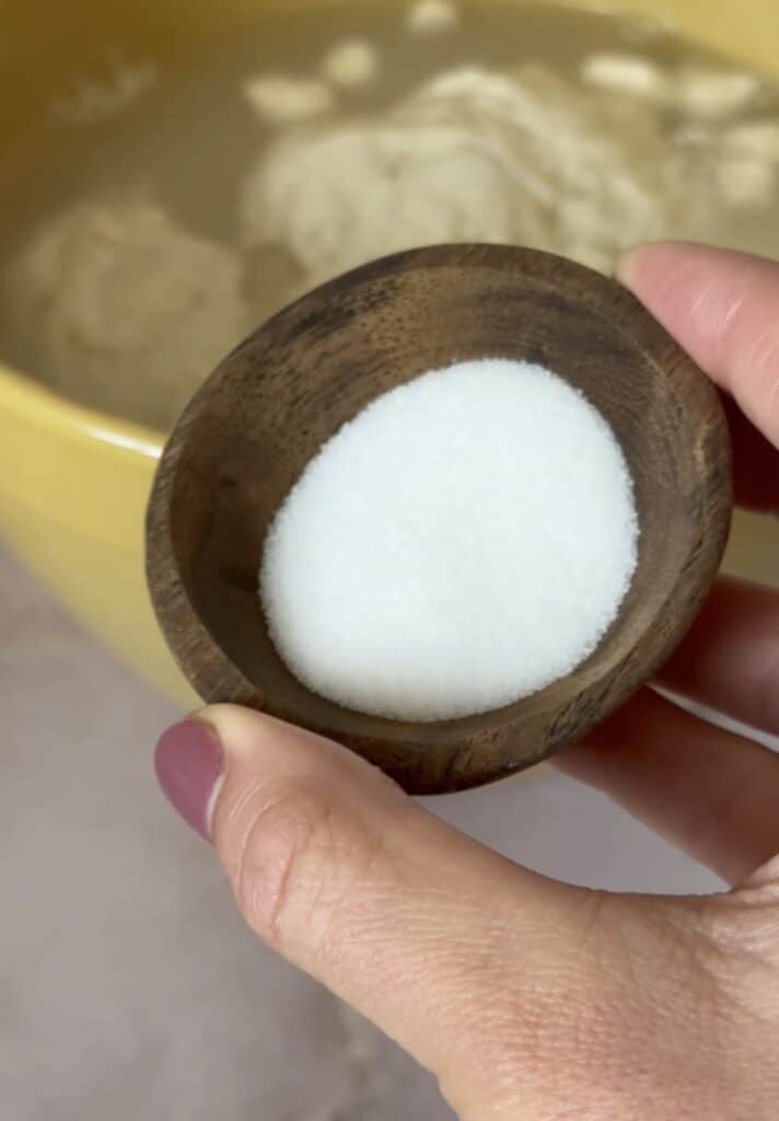 hand holding a small bowl of salt over a larger bowl of sourdough dough.