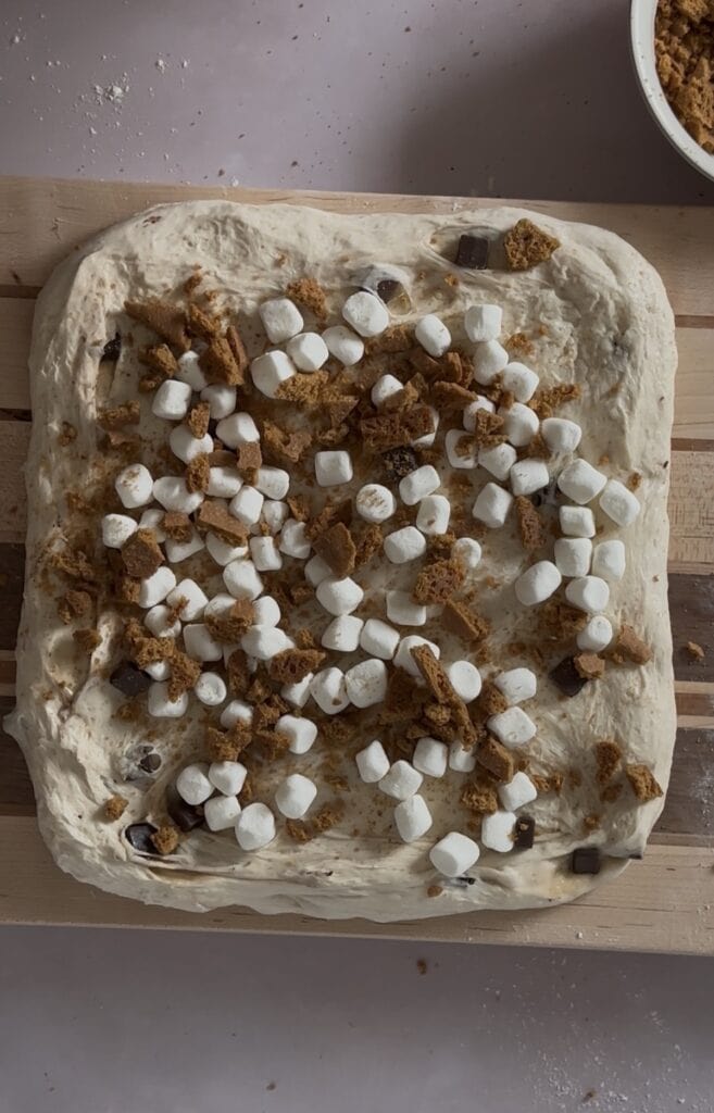 Homemade S'mores sourdough dough spread out into a large square and topped with marshmallows and graham crackers.