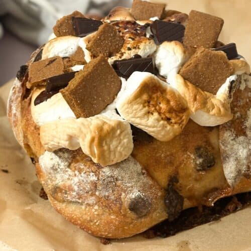 A loaf of s'mores sourdough bread topped with roasted marshmallows, graham crackers and chocolate pieces.