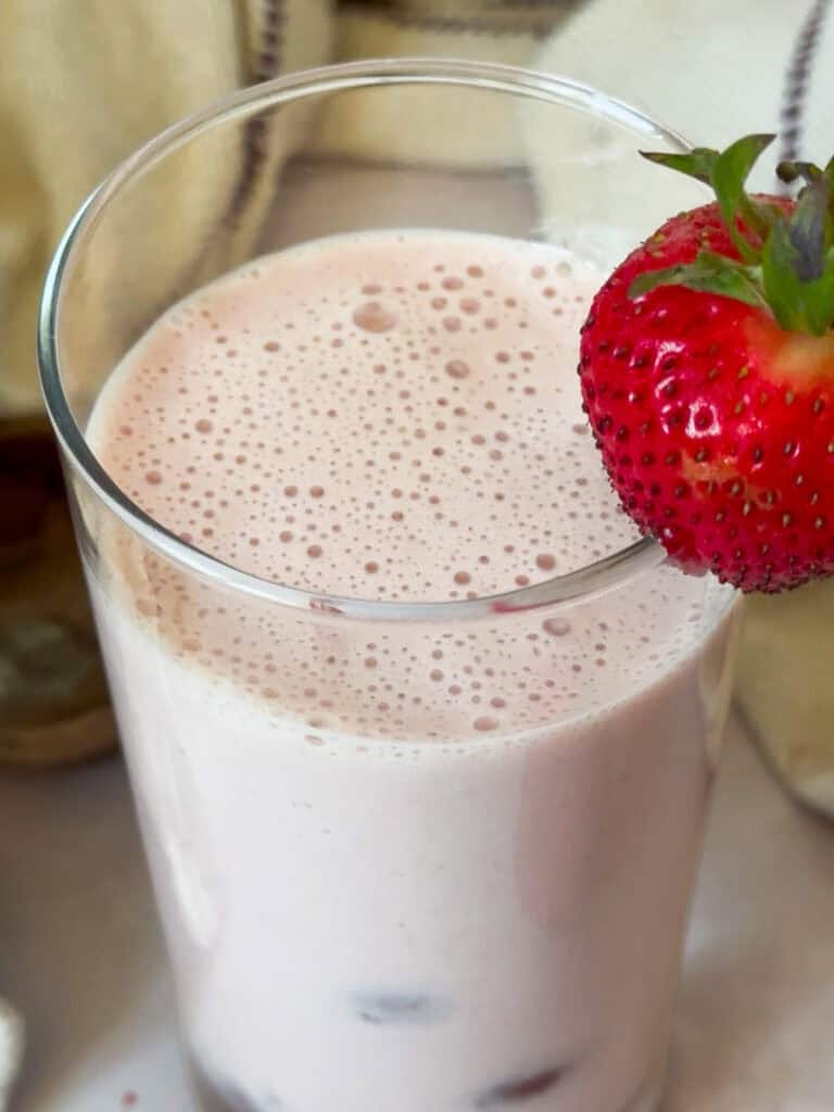 strawberry milk in a glass and garnished with a fresh strawberry.
