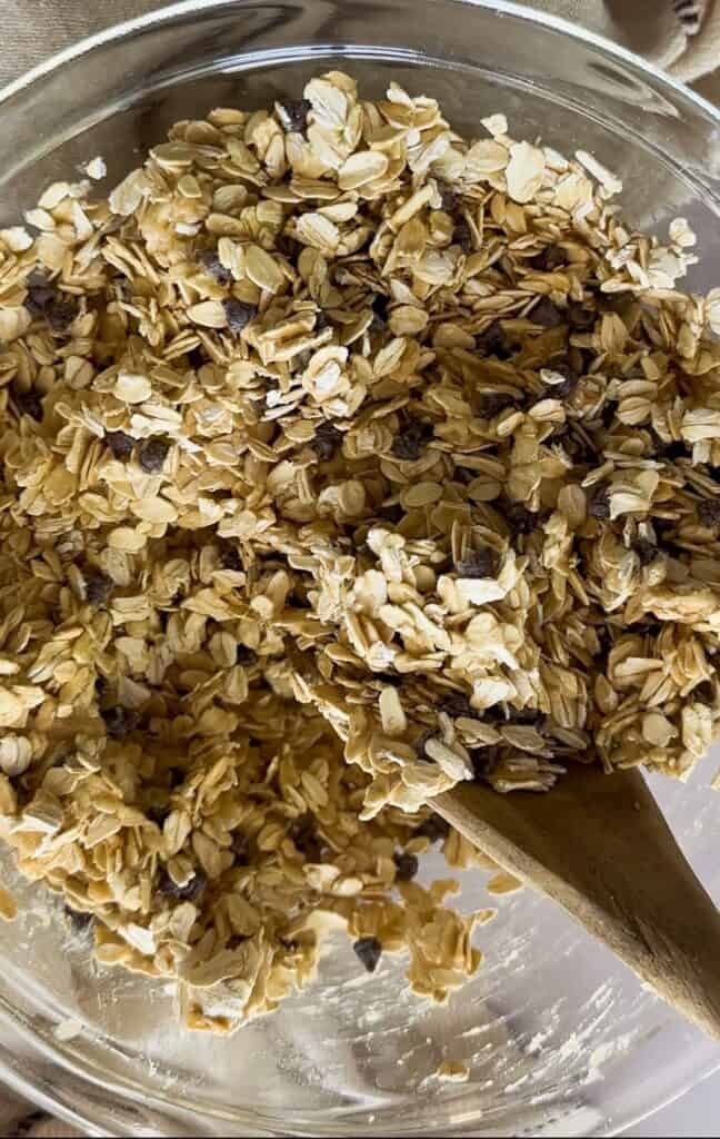 sourdough granola in mixing bowl being stirred together with a wooden spoon. 