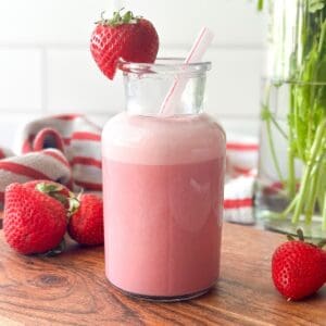 strawberry milk in a small glass with a strawberry on the rim for garnish.