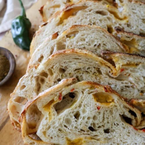 sourdough green chile cheddar bread sliced on a cutting board.